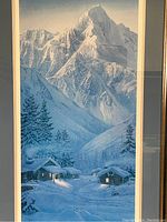 Close-up showing the winter mountain scene with lit log cabins, snow covered pine trees, and detailed mountain background in blue tones.