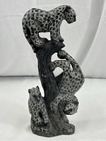 Front view of the stone sculpture showing all three leopards in different climbing positions on the tree stump base.