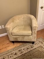 Front view of golden microfiber barrel chair on wooden floor beside a wall and floral rug.