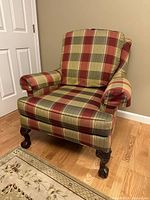 Front angle view of plaid upholstered accent chair showing green and burgundy pattern with padded armrests and claw foot legs.