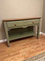 Full view of olive green accent table against wall on wood floor, showing drawer and lower shelf.