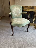 Full view of the antique Louis XVI style walnut armchair with green floral needlepoint upholstery placed on carpet in front of fireplace.