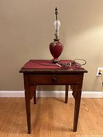 Front view of antique burgundy wooden table with ceramic burgundy lamp on top, showing table drawer knob and lamp bulb fitting.