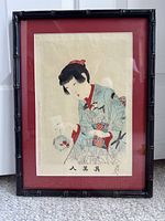 Frontal image of the framed woodblock print showing the young beauty in kimono holding a small bowl with a goldfish, mounted with red matboard and black bamboo frame.