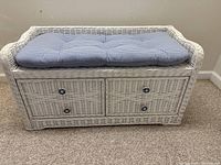 Front view of white wicker bench with blue and white gingham cushion and two drawers with decorative knobs.