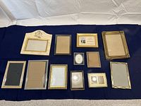Full display of all 12 assorted picture frames laid on blue fabric background, various shapes and sizes.