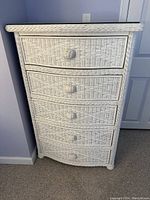 Front view of white wicker tall chest with five drawers and wicker knobs.