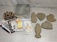 Overview showing the cookie art set contents including the brown pressed fiberboard molds, metal storage tin, paint brushes, and four instructional books.