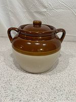 Front view of a two-tone brown and beige glazed Boston Baked Bean pot with lid on, showing rounded handles and smooth glossy finish.