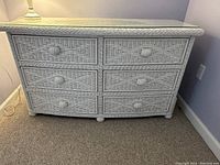 Front view of the white wicker dresser showing six drawers, each with woven fronts and round woven knobs.
