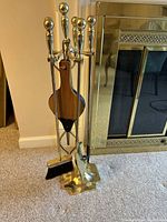Brass metal 6-piece fireplace tool set with stand, showing tools arranged in the stand near the fireplace.