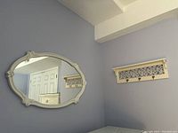 White framed oval mirror with decorative corners hanging on a blue wall near the coat rack.
