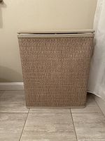 Front view of beige hamper with vinyl top and woven textured base on tiled floor