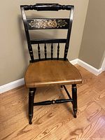 Front view of the Hitchcock black maple chair showing the scooped natural wood seat and floral painted top rail.