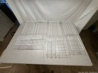 Top view of nine white wire rack shelves arranged on carpeted floor showing size variation and open wire grid construction.