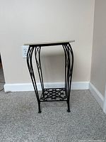 Iron rod plant stand with curved legs, decorative bottom shelf, and square beige tile top.