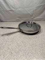 Full side view of stainless steel skillet with lid on granite countertop.