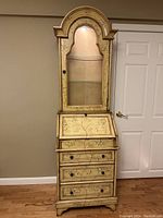 Full front view of the two-piece secretary desk with closed drop front and lighted glass door bookcase cabinet above, showing floral painted design and arched top of cabinet