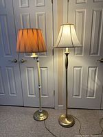 Both floor lamps shown side by side, one with cream folded fabric column and brass base, the other gold tone with cream shade.