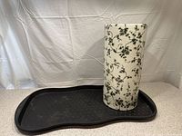 Porcelain umbrella stand to the right and black plastic boot mat to the left on a light backdrop, clearly showing size and condition of both items.