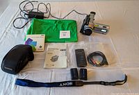 Sony Digital Handycam video camera with its accessories spread on a surface showing green screen, batteries, manual, remote control, cables, camera case, and software package.