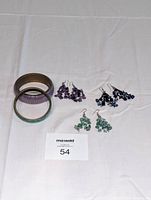 Photo showing two metal bangle bracelets with patina alongside three pairs of cluster bead drop earrings in purple, dark blue, and light green.