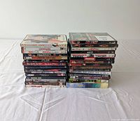 Photo of 30 DVD cases stacked in two piles on white surface, showing spines and some front covers with visible titles.