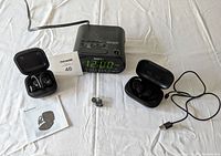 Lot showing all items including two pairs of Bluetooth earphones in cases, Sony alarm clock, charging cable, manual, and spare ear tips.