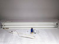 Fluorescent strip light fixture with two fluorescent tubes and power cord laid flat on a white surface.