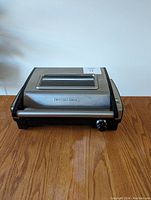 Front view of Hamilton Beach indoor electric grill showing stainless steel lid with clear window, brand name on front, and control knob on right side.