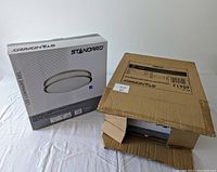 Two boxes, one partially open showing the boxed light fixture. The boxes are white and grey with STANDARD brand and image of the light fixture on front.