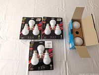Three unopened packs each with 3 FEIT Electric LED dimmable 60W warm white bulbs, plus one opened box with 2 Ecosmart LED 60W daylight bulbs visible inside.