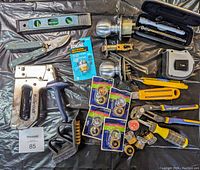 Overview of miscellaneous tools including Mastercraft staple gun, fuses, level, pliers, door handle, and more on a black surface.