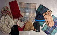 Overview photo of all 12 items including scarves, toques, mittens, and visor laid out on a surface with a white background.
