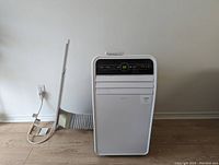 Front view of white Insignia portable air conditioner unit connected to exhaust hose and window vent panel, showing control panel and digital display at 56 degrees.