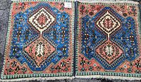 Two matching oriental rugs side by side showing their geometric and floral designs with blue, coral, cream, and black colors and fringed edges.