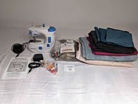 Photo showing the full lot with Dressmaker II sewing machine, power accessories, instruction manual, assorted fabric pieces, and sewing accessories including spools of thread and small tools.