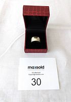 Wide silver band ring placed inside open red textured jewelry box with black interior background.