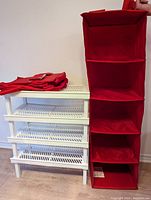 White collapsible shoe rack with three plastic slotted shelves and two red fabric hanging closets, one hanging with compartments visible.
