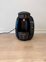 Front view of Bosch Tassimo coffee maker showing the pod brewing area, collection cup with logo, and branded front panel