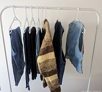 Full view of clothing items on white clothing rack including two denim vests, jeans, skirt, and brown striped sweater