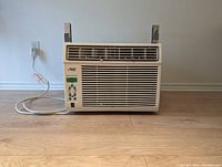 Frontal view of Arctic King window air conditioner showing front grille, control panel, power cord, and wooden brackets taped to sides.