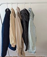 Side view of five women's jackets hanging on a rack, showing different colors and materials