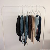 Photo showing 8 pairs of women's pants and jeans hanging on a garment rack, some black, blue, brown, and other colors.