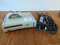 White Xbox 360 console with one white wireless controller on top, power supply and composite AV cable to the right.