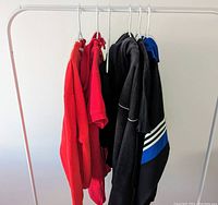 Six youth sports clothing items hung on white rack showing variety of colors and styles.