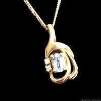 Close-up of pendant showing oval aquamarine and three diamonds against black background