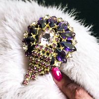 Front view of 1950s vintage amethyst rhinestone brooch held against light-colored fabric, showing purple marquise and round clear rhinestones with cascading small rhinestones and gold-tone metal.