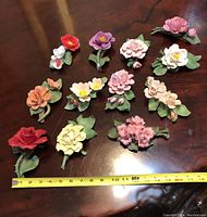 Full view of 12 hand-painted porcelain flowers arranged with tape measure showing sizes.
