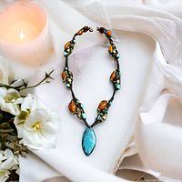 Necklace laid on white cloth near flowers and candle showing full piece and details